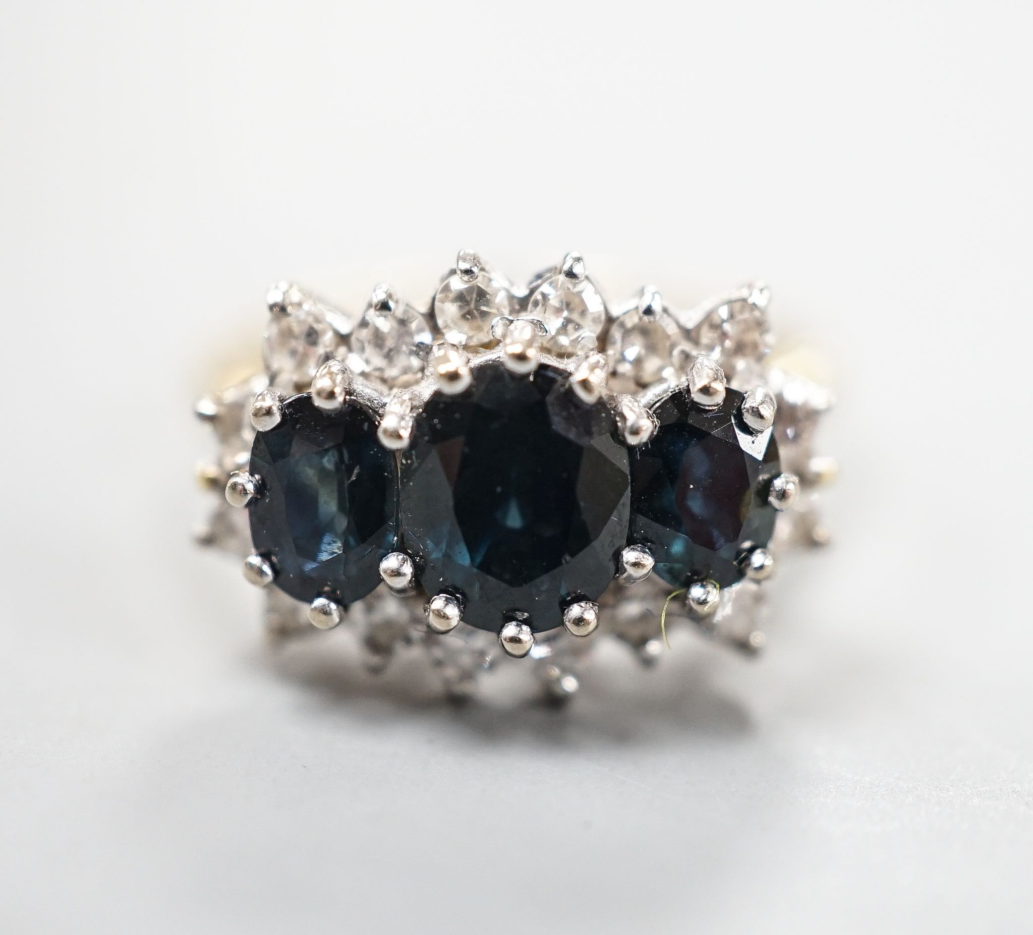 An 18ct and three stone sapphire set ring with diamond set border, size O, gross weight 5.3 grams.